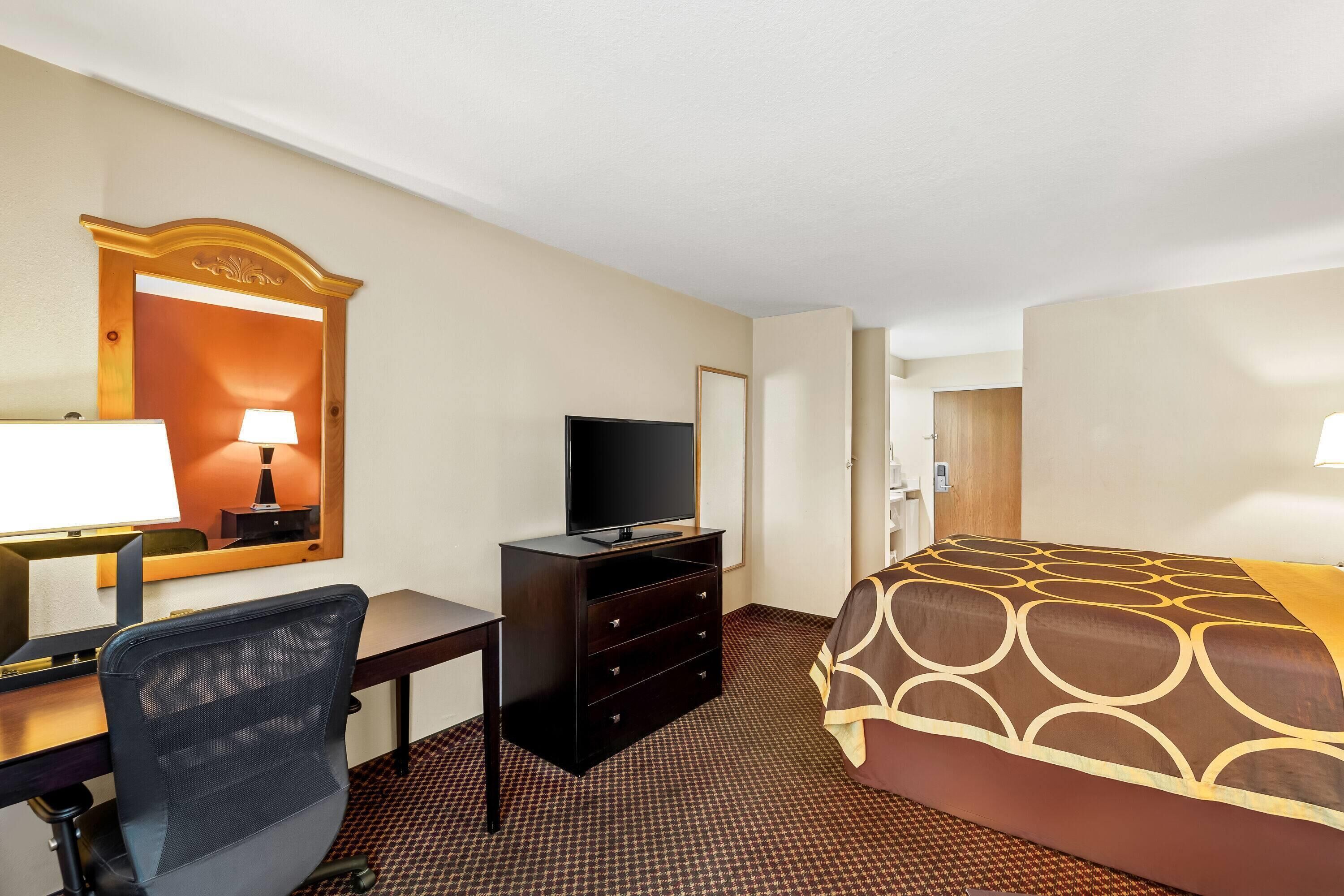 A hotel room with a bed, desk, chair, television, dresser, and a mirror.