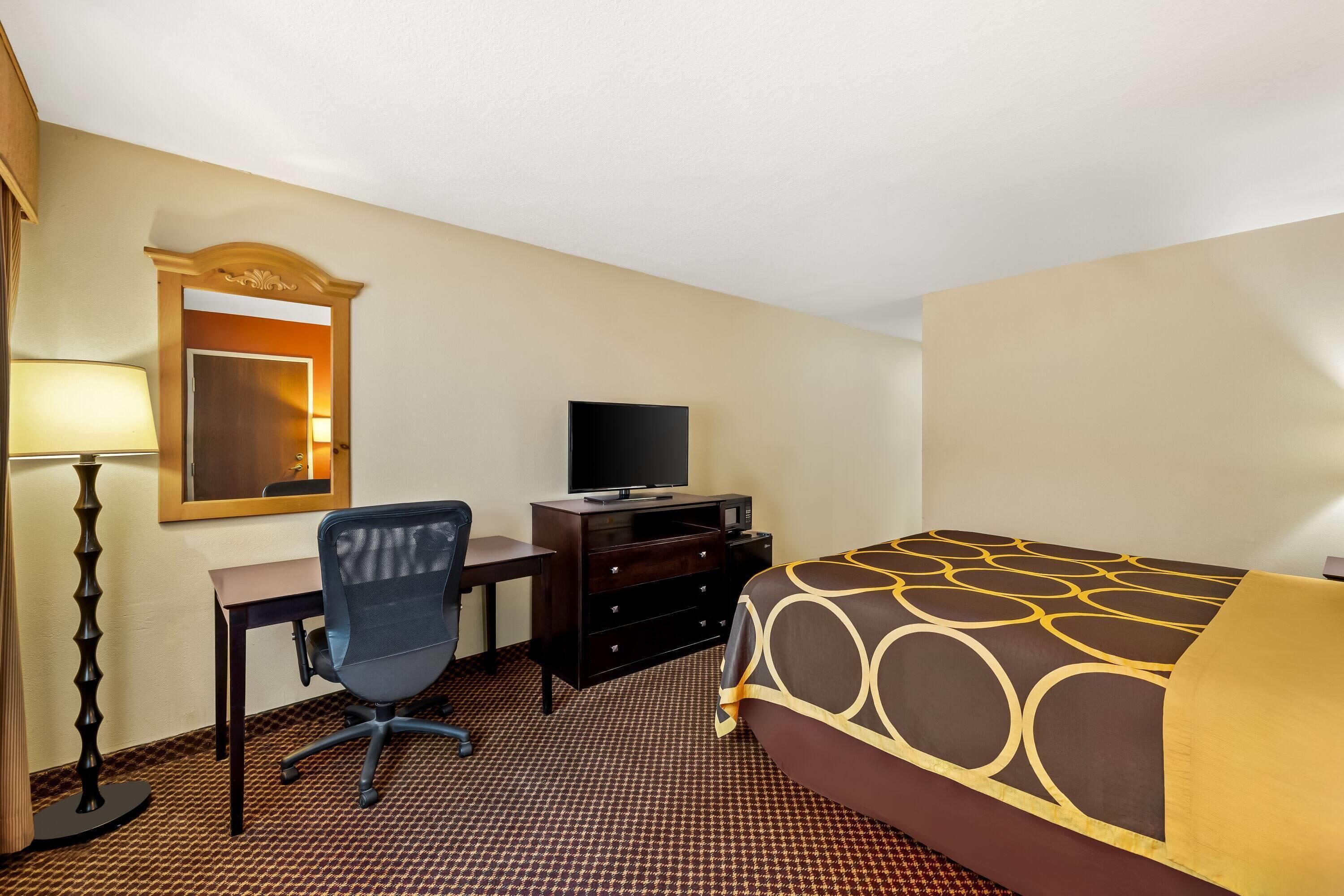 A hotel room with a bed, desk, chair, television, and dresser.