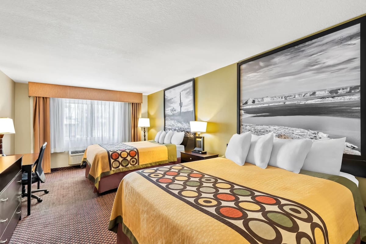 A hotel room with two beds, a desk, and a large window with curtains.