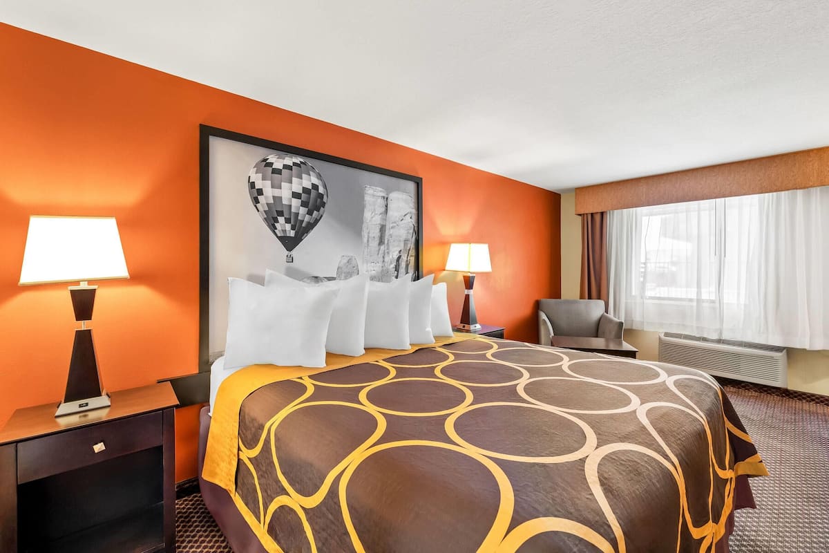 A hotel room with a large bed, two bedside tables with lamps, a chair, a window with curtains, and a framed picture on the wall.