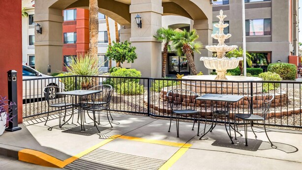 An outdoor patio with tables and chairs, a fountain, and a building with multiple floors and balconies in the background. - Super 8 by Wyndham Marana/Tucson Area (Tucson)