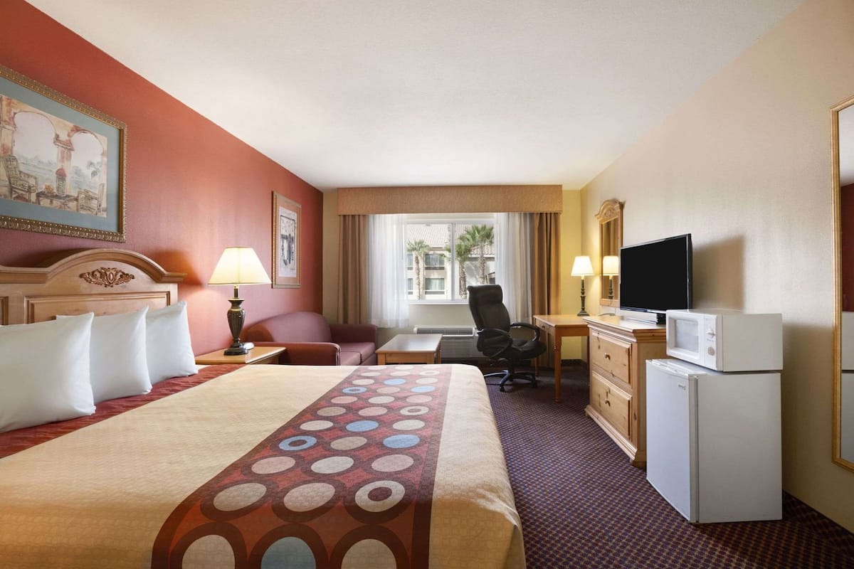 A hotel room with a bed, a desk, a chair, a television, and a microwave.