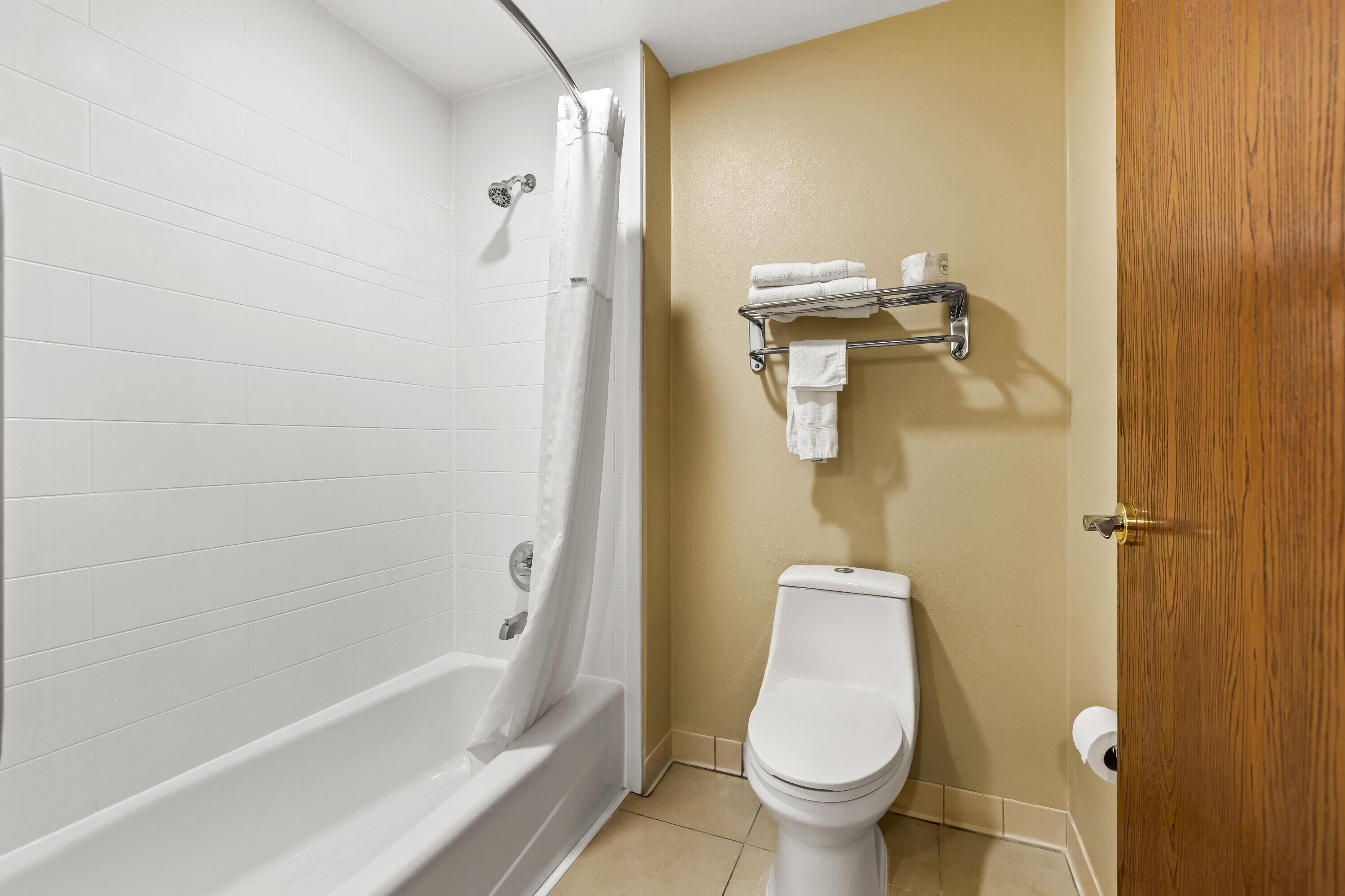 A bathroom with a white bathtub, a toilet, and a wooden door.
