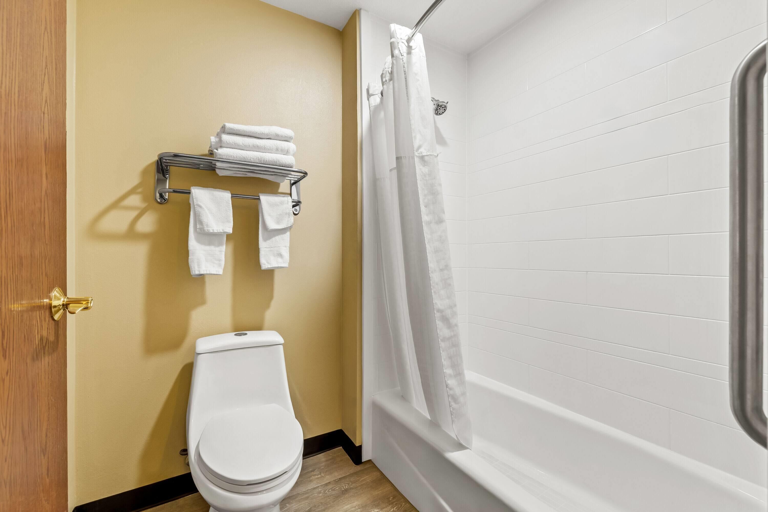 A bathroom with a toilet, a towel rack with folded towels, a shower curtain, and white tiled walls.