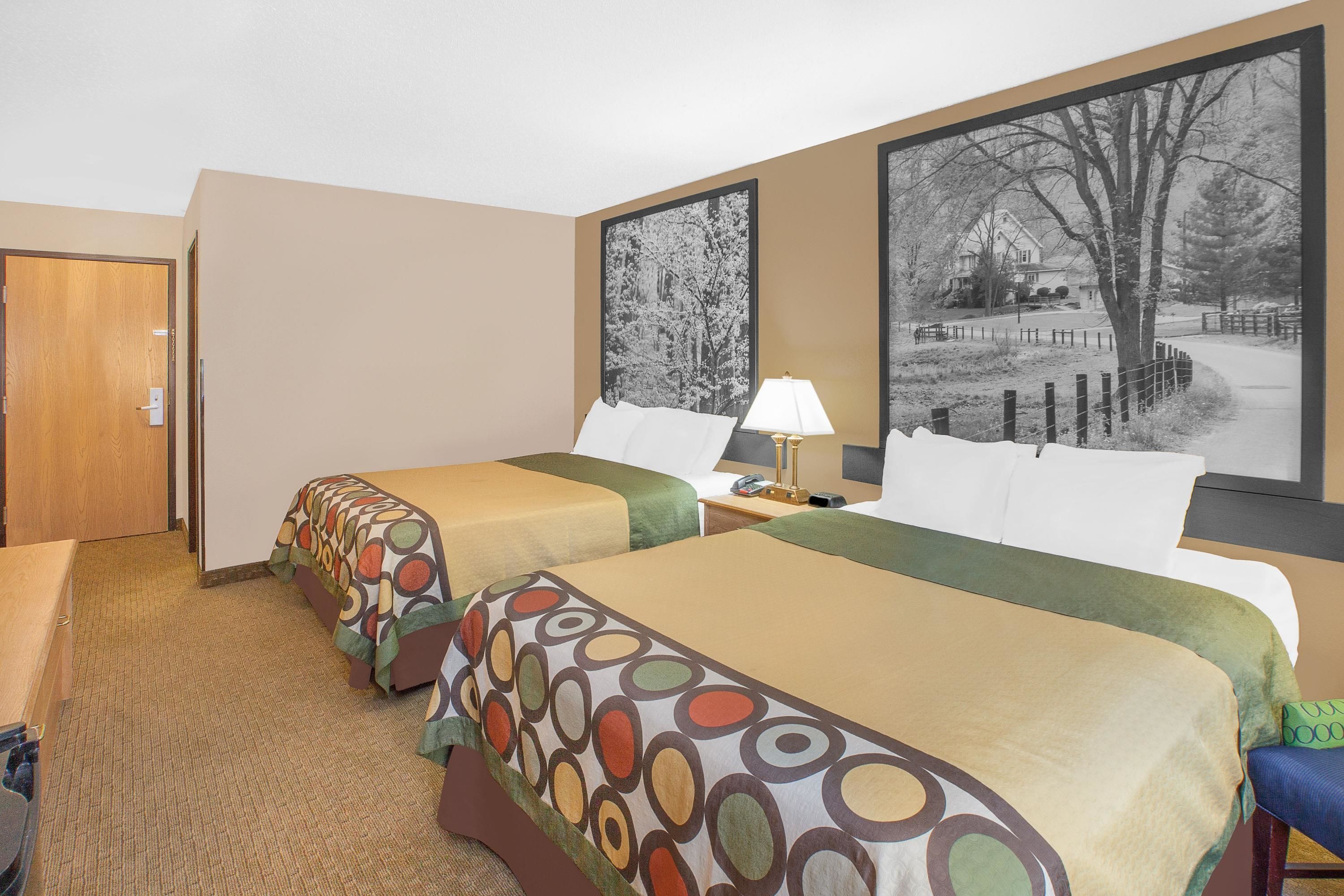 Habitación de hotel con dos camas, una mesita de noche con lámpara, y dos fotografías grandes en blanco y negro en la pared.
