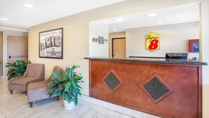Zona de recepción de un hotel con un mostrador de madera, dos sillones estampados, un gran cartel de bienvenida enmarcado y el logotipo de Super 8 en la pared.