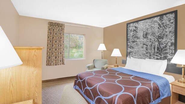 Habitación de hotel con una cama grande, dos lámparas de noche, una silla, una ventana con cortinas y un cuadro enmarcado en la pared.