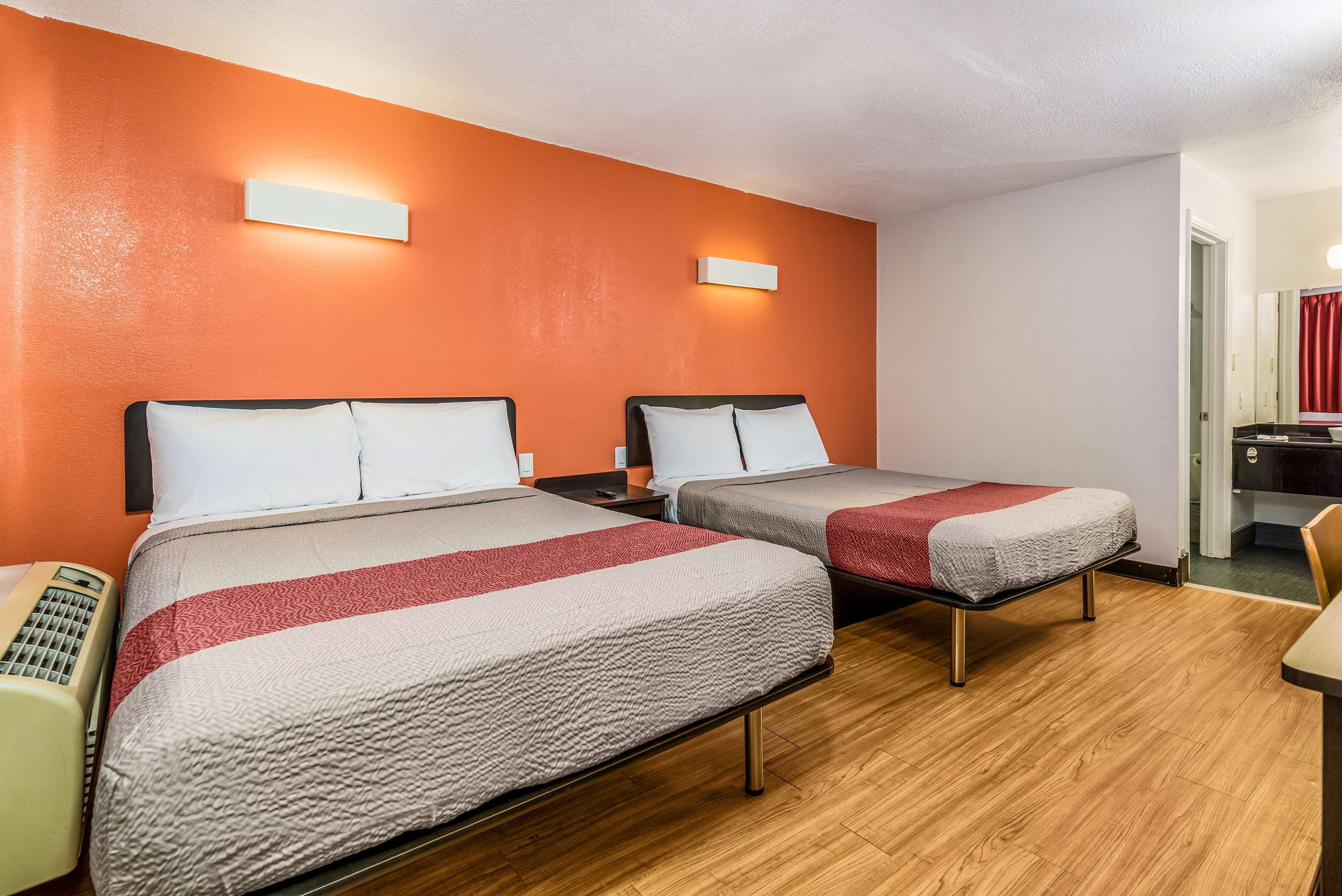 Een hotelkamer met twee bedden, een houten vloer en een rode accentmuur.