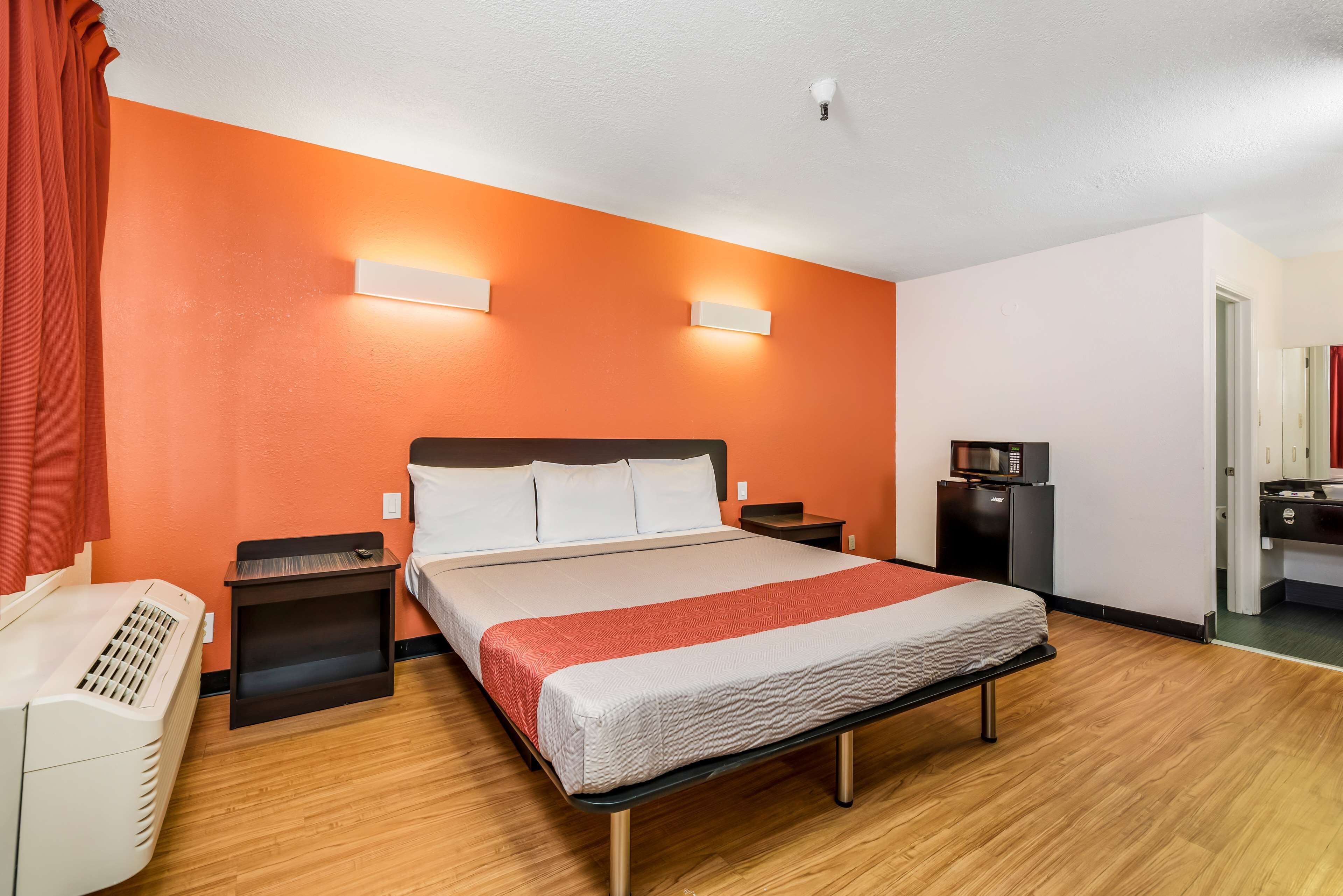 A hotel room with a large bed, two bedside tables, a heater, a microwave, and a small kitchenette.