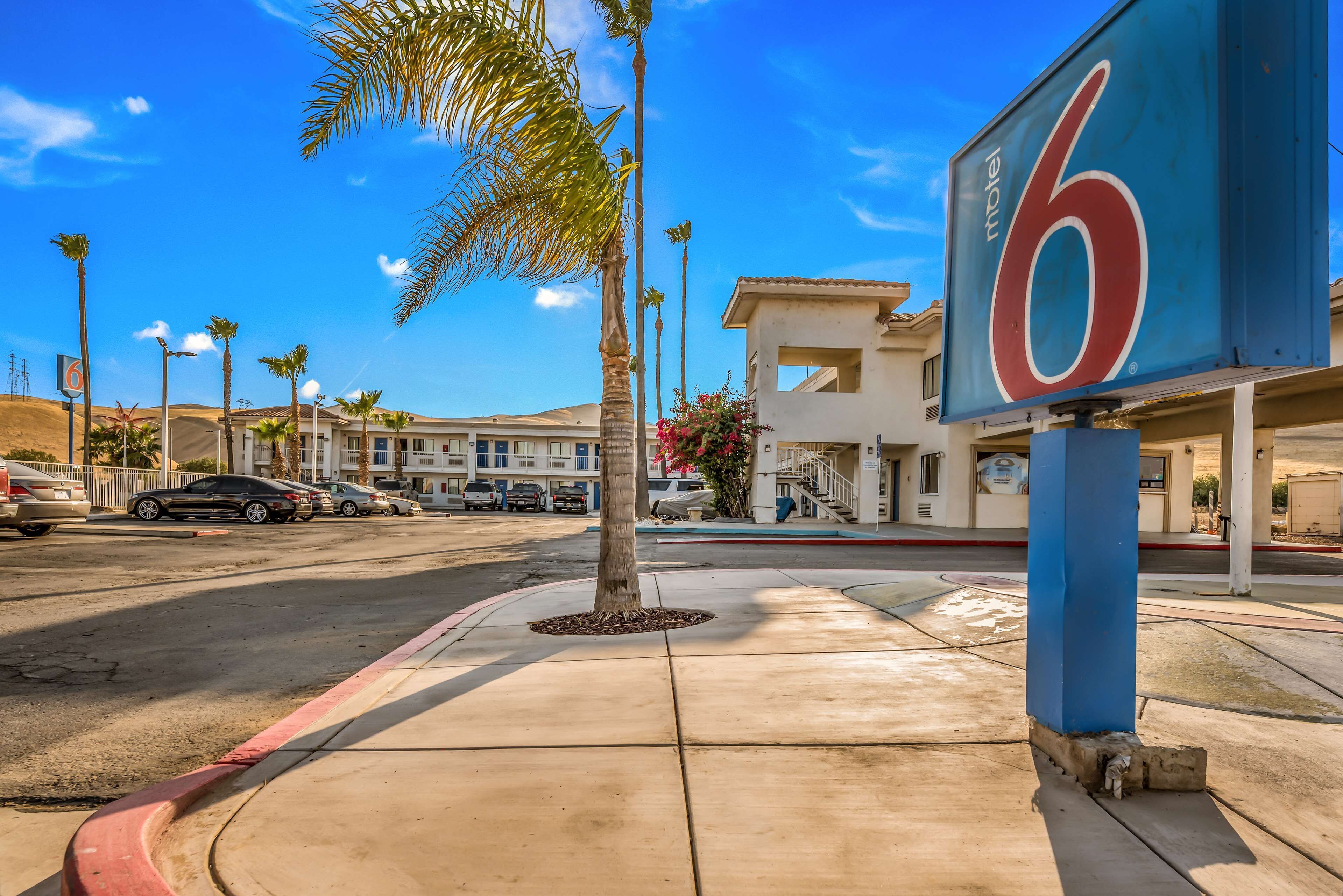 Un motel avec un grand panneau indiquant le chiffre « 6 », des palmiers et un parking rempli de voitures.