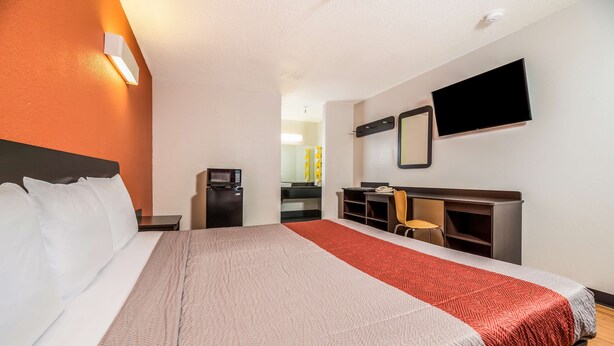 Una camera d'albergo con un letto, una scrivania, una sedia, una TV e un forno a microonde.