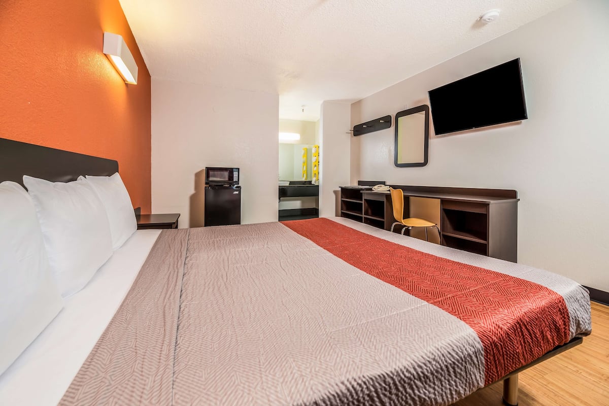 A hotel room with a bed, a desk, a chair, a TV, and a microwave.