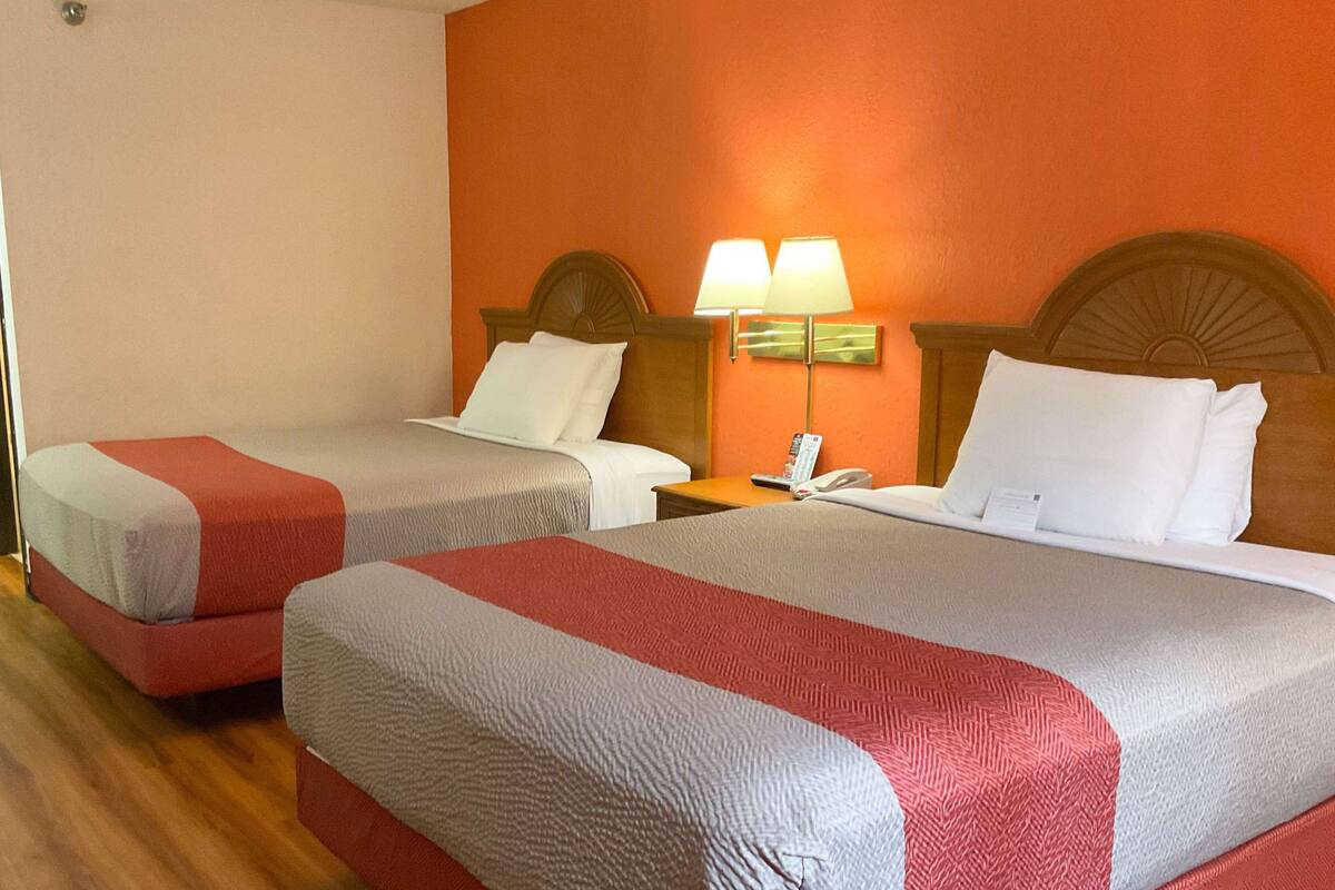 A hotel room with two beds, each with a red and white bedspread, a wooden headboard, and a nightstand with a lamp and phone.