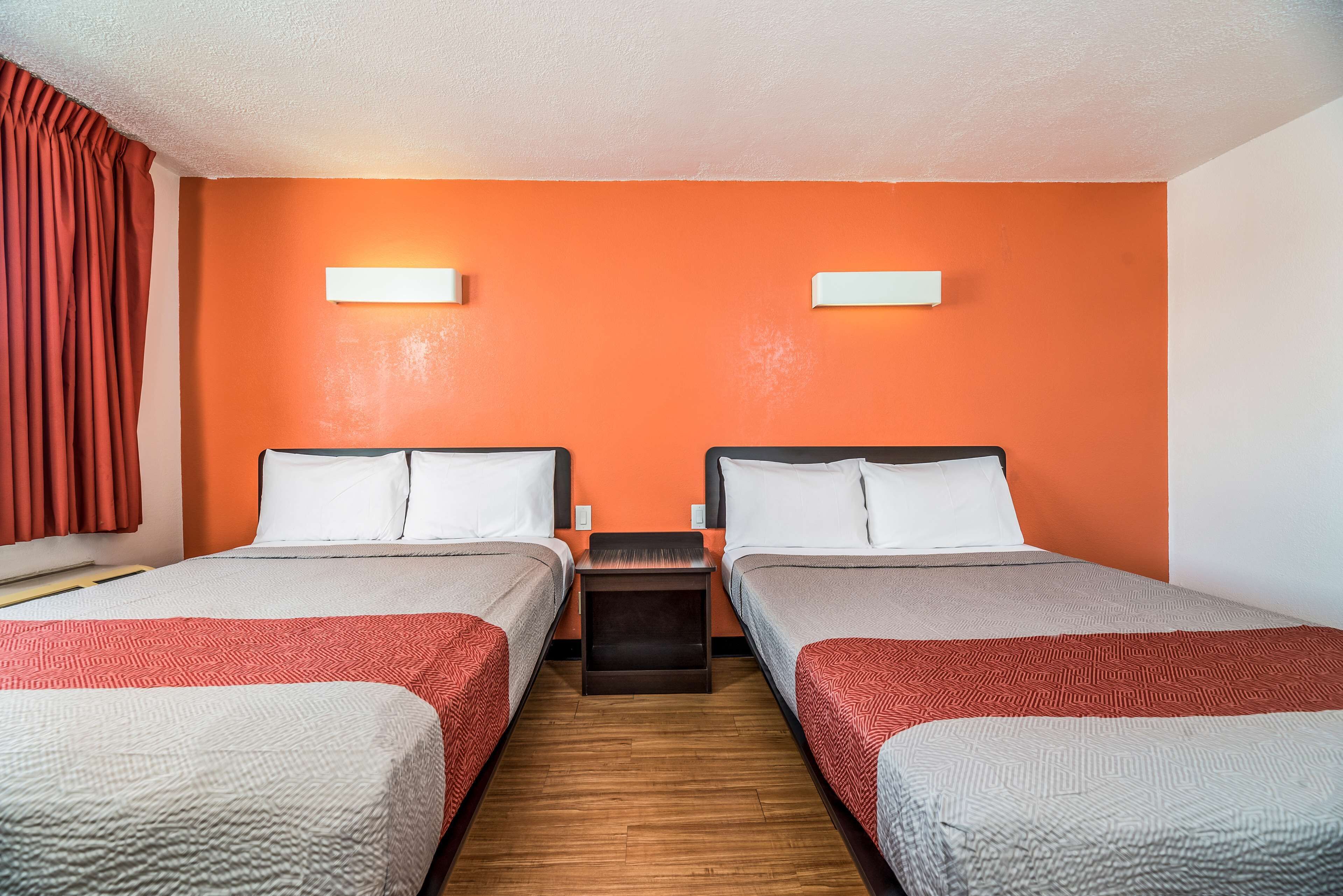 Une chambre d’hôtel avec deux lits, des murs orange et un plancher en bois.