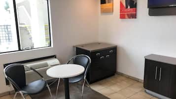 A small, modern room with a round table and two chairs, a cabinet with drawers, a radiator, and a window with a view of a building outside.