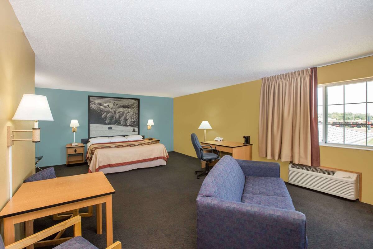 Une chambre d’hôtel avec un lit, un bureau, une chaise, un canapé et une fenêtre avec des rideaux.