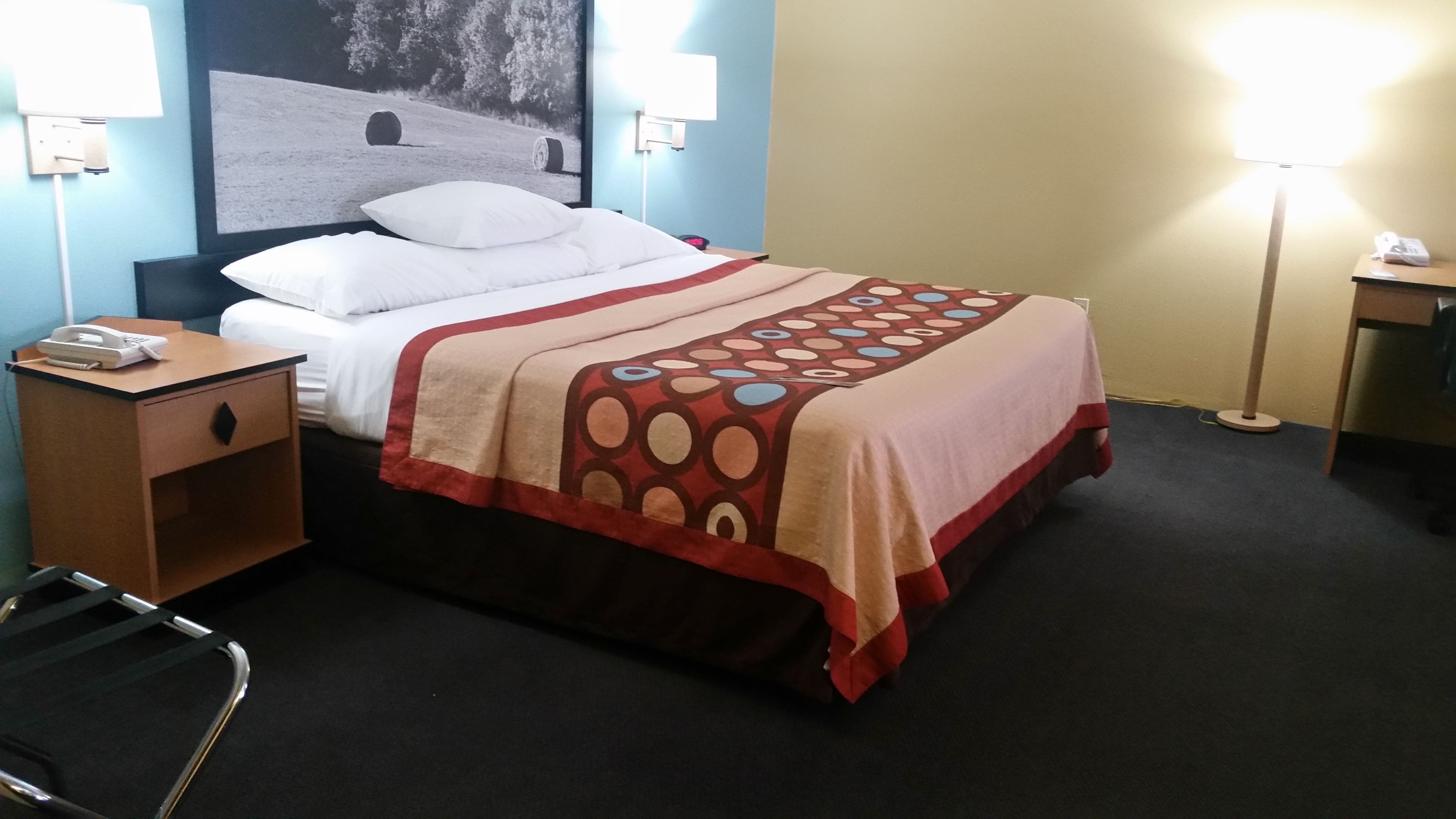 A hotel room with a bed, a bedside table with a phone, a chair, and a lamp.
