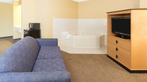 A hotel room with a sofa, a television, a bathtub, and a small desk with a microwave. - Super 8 by Wyndham Clarinda (Clarinda)