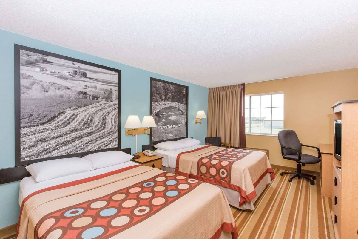 Une chambre d’hôtel avec deux lits, un bureau, une chaise, une télévision et deux lampes fixées au mur.
