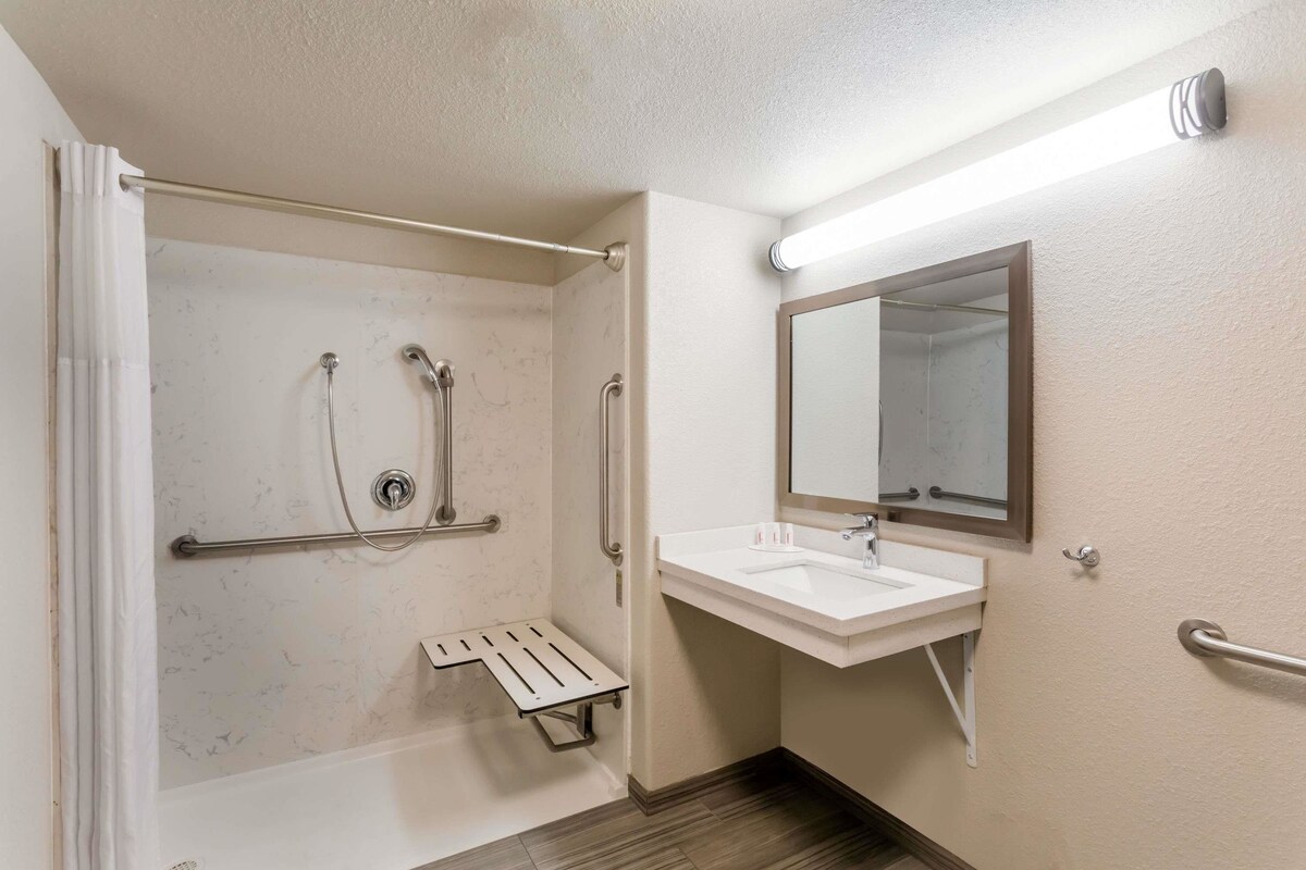 Une salle de bain équipée d’une douche, d’un lavabo, d’un miroir et de barres d’appui.