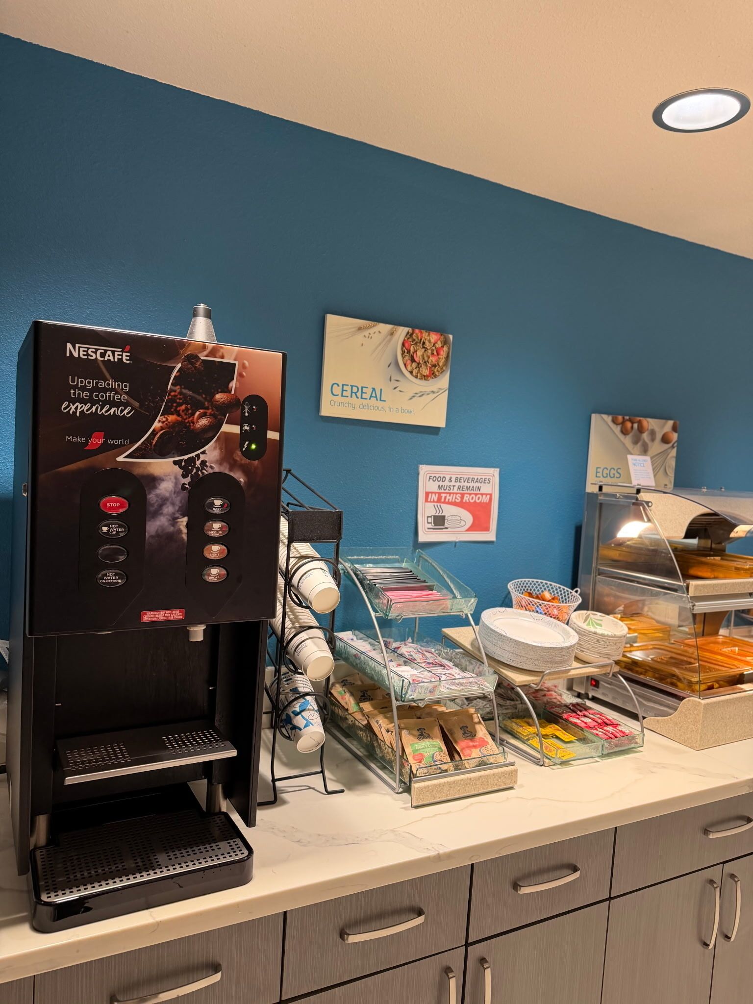 A coffee station with a Nescafe machine, cereal display, and a sign indicating food and beverages must remain in the room.
