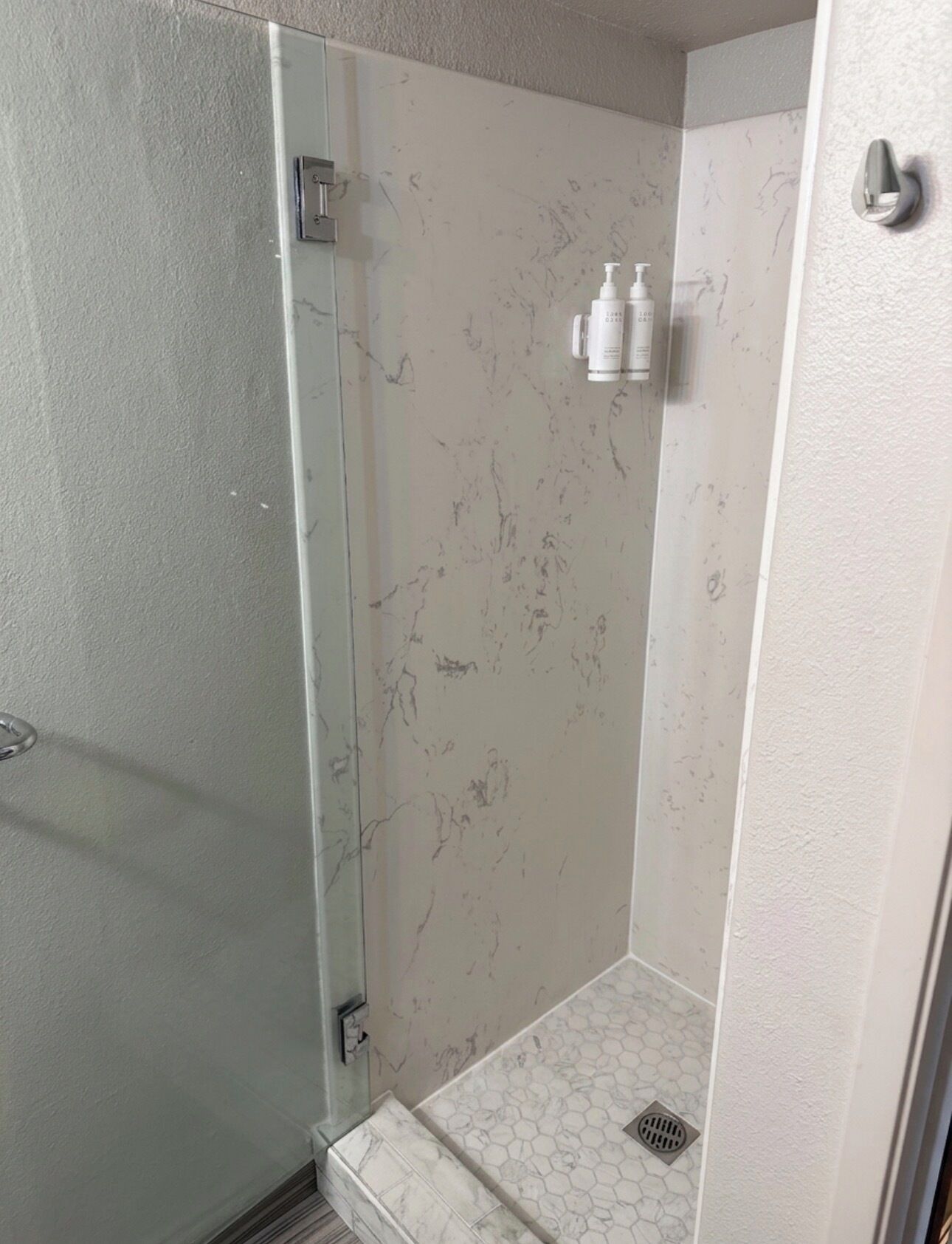 A shower with a glass door, a marble wall, and a small shelf with toiletries.