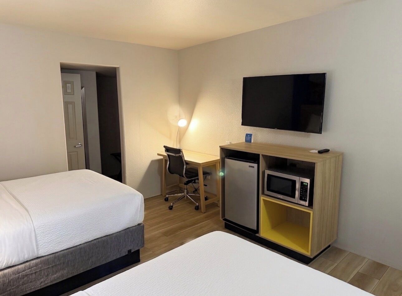A hotel room with two beds, a desk, a television, a refrigerator, and a microwave.