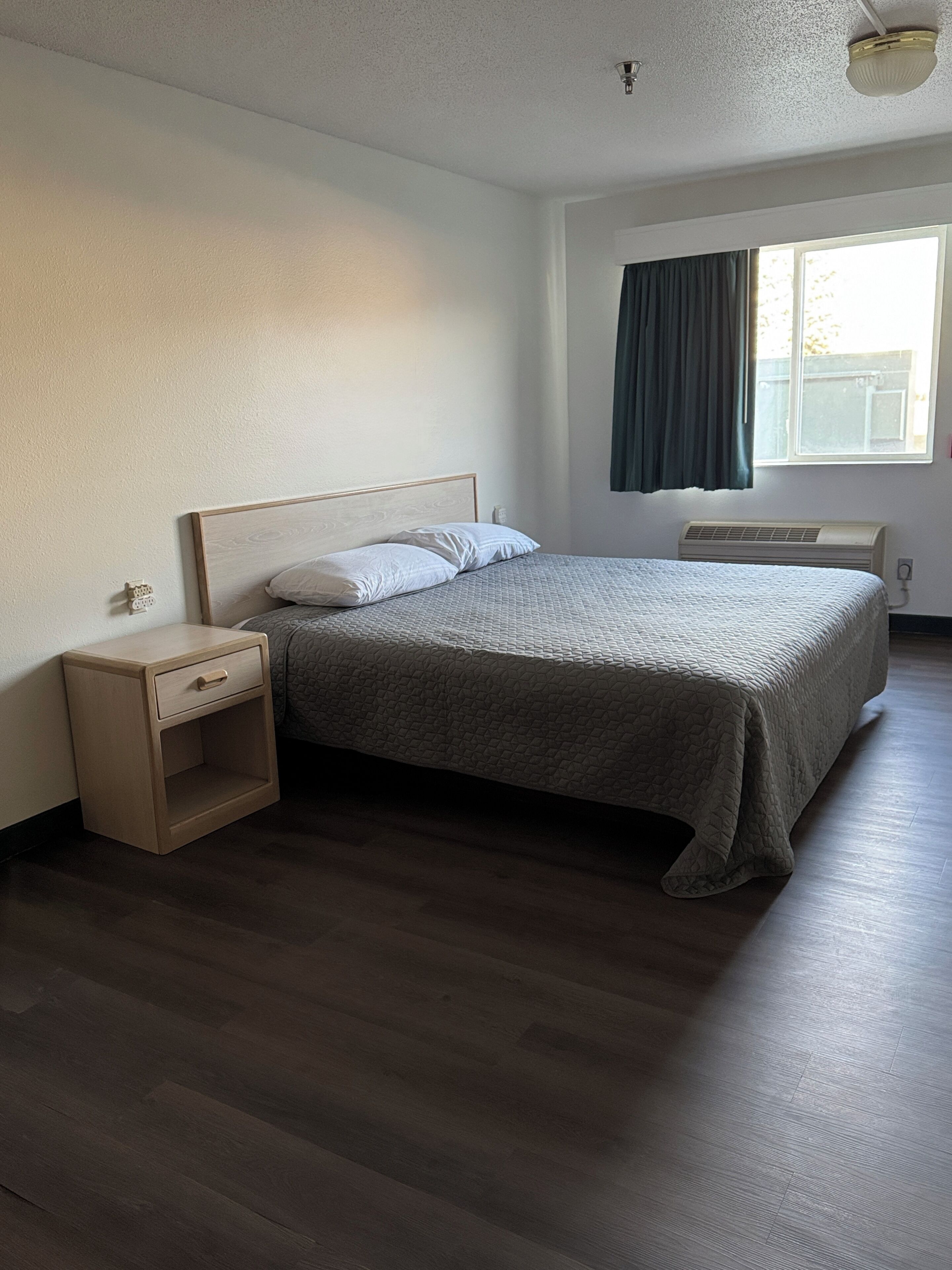 Une chambre à coucher avec un lit, une table de chevet, une fenêtre avec des rideaux et un ventilateur de plafond.