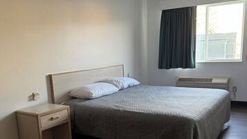 Une chambre à coucher avec un lit, une table de chevet, une fenêtre avec des rideaux et un ventilateur de plafond.