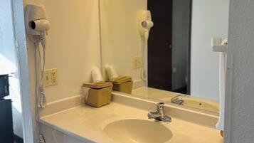 A hotel bathroom with a white sink, a mirror, a hairdryer, and a towel dispenser.