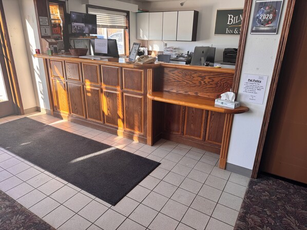 A reception desk with a wooden finish, a digital screen, and a sign indicating pet policy. - Bilmar Inn & Suites Dell Rapids Near Sioux Falls (Dell Rapids)