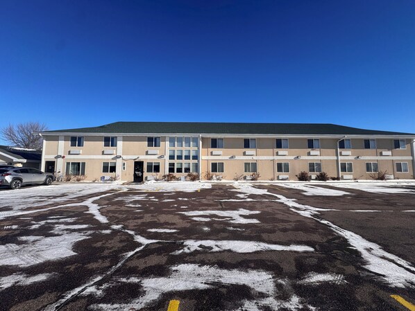 A multi-story building with a flat roof and a parking lot with snow patches. - Bilmar Inn & Suites Dell Rapids Near Sioux Falls (Dell Rapids)