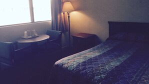 A hotel room with a bed, a small round table with a chair, a lamp, and a window with curtains. - Red Carpet Inn (Gloucester City)