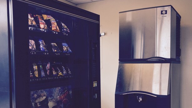 A vending machine with various snack options and a stainless steel refrigerator. - Red Carpet Inn (Gloucester City)