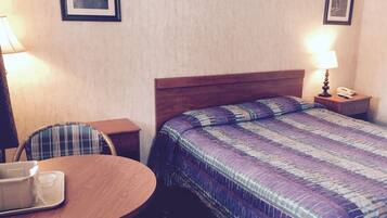 A hotel room with a wooden bed, a round table with a chair, a lamp, and a framed picture on the wall.