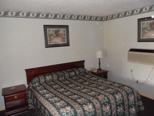 A bedroom with a bed, a nightstand, a lamp, and two framed pictures on the wall.
