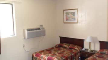 A hotel room with two beds, a wall-mounted air conditioner, a bedside lamp, and a framed picture on the wall.