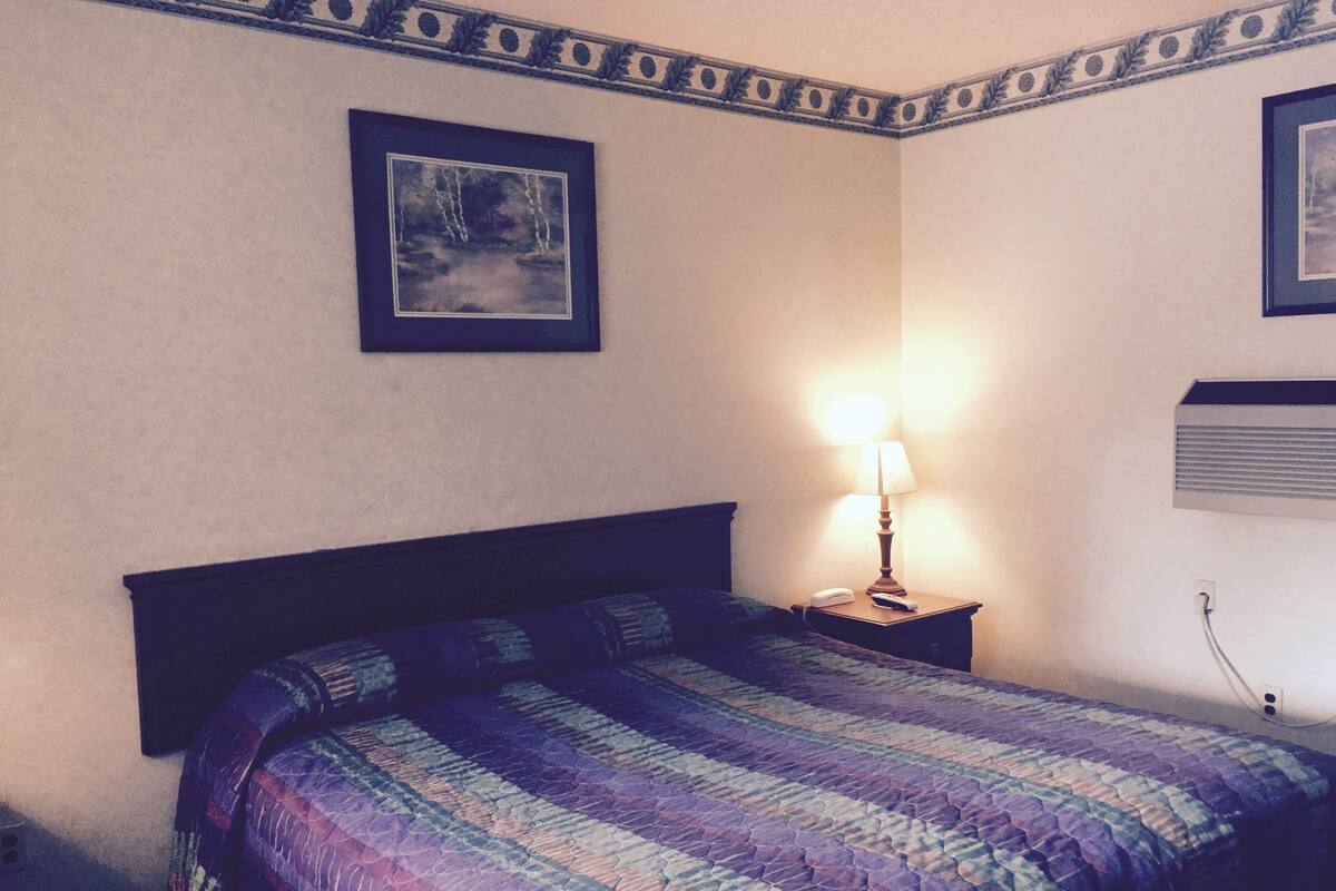 Una camera da letto con un letto, un comodino con una lampada e un condizionatore d'aria a parete.