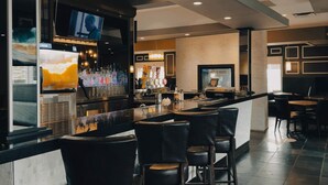 A bar area with a counter, multiple bar stools, and a television screen mounted above the bar.