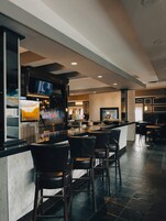 Una zona de bar con mostrador, varios taburetes altos y una pantalla de televisión sobre la barra.