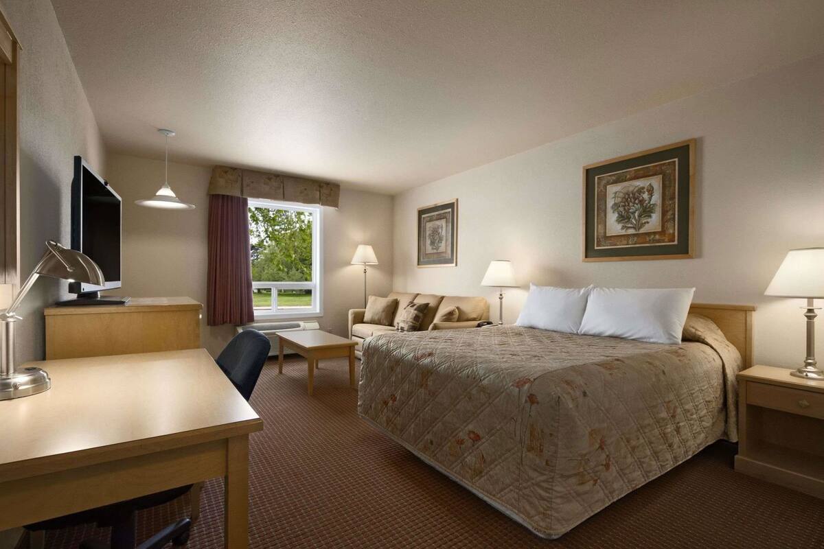 Ein Hotelzimmer mit Bett, Schreibtisch, Stuhl, zwei Lampen, einem Fernseher und gerahmten Bildern an den Wänden.