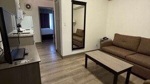 A compact living space with a kitchenette, a sofa, a coffee table, and a mirror.