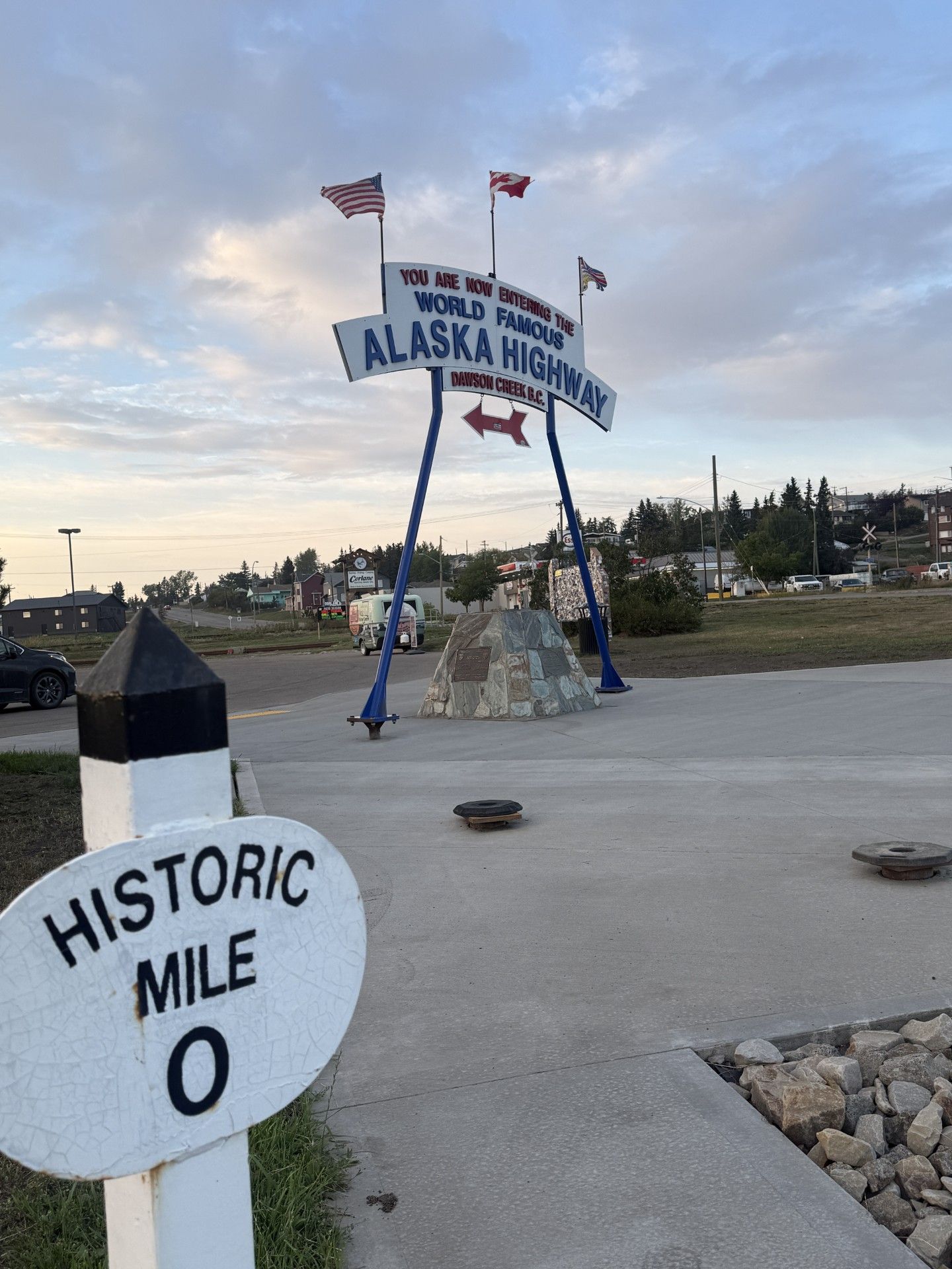 A historic mile marker sign and a welcome sign for the Alaska Highway.