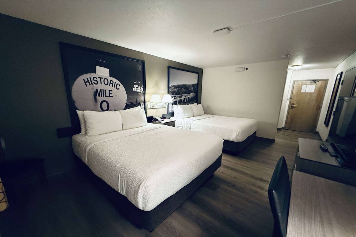 Ein Hotelzimmer mit zwei Betten, einem Schreibtisch, einem Stuhl, einem Fernseher und einer großen Wanduhr.