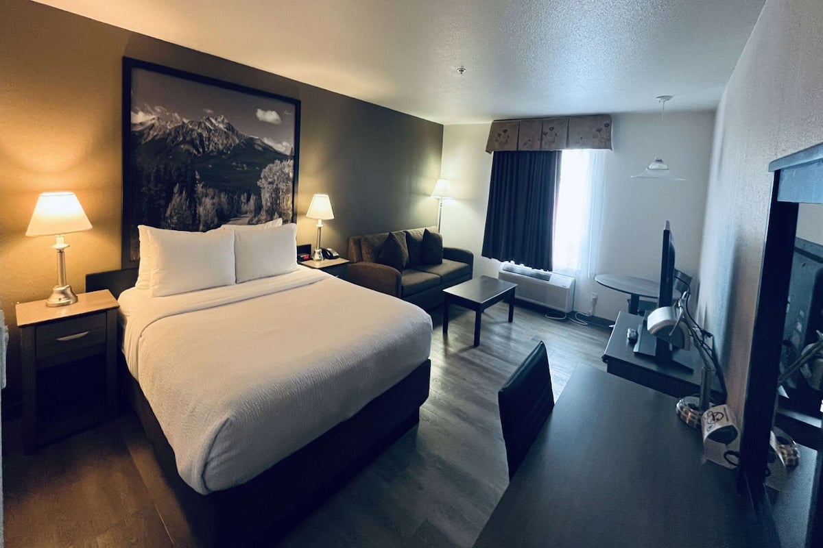 Ein Hotelzimmer mit einem großen Bett, zwei Nachttischen mit Lampen, einem Sofa, einem Couchtisch und einem Fernseher.