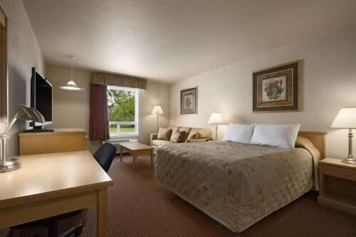 Ein Hotelzimmer mit Bett, Schreibtisch, Stuhl, Fernseher und zwei Lampen.