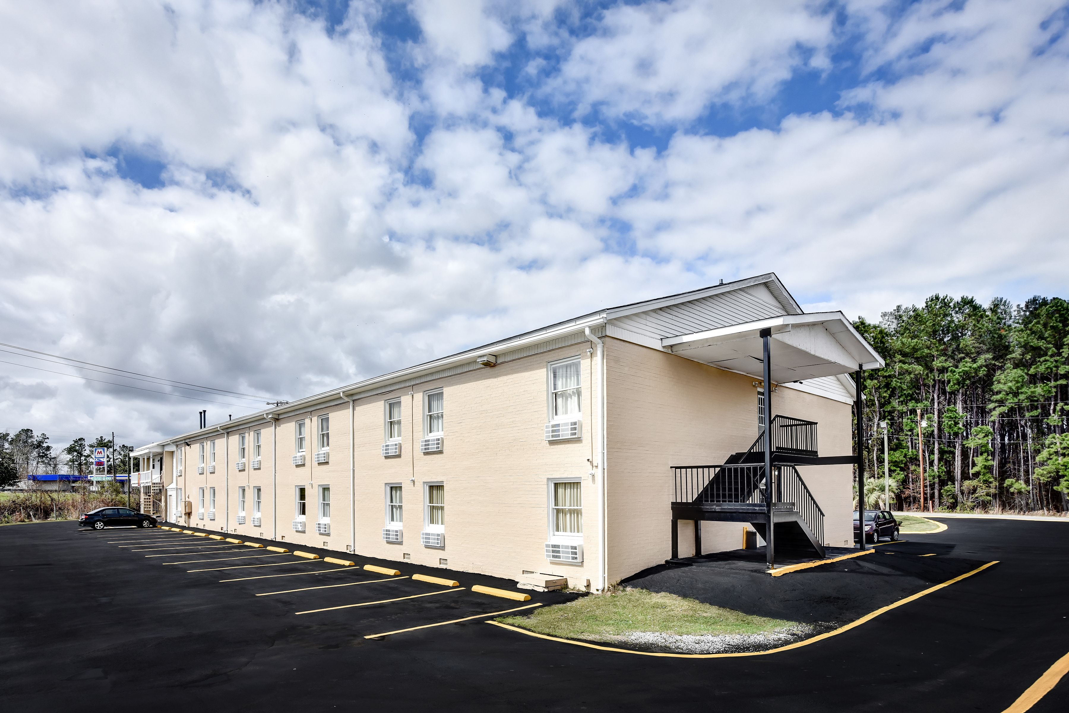A motel with a parking lot, a covered walkway, and a staircase leading to the building.