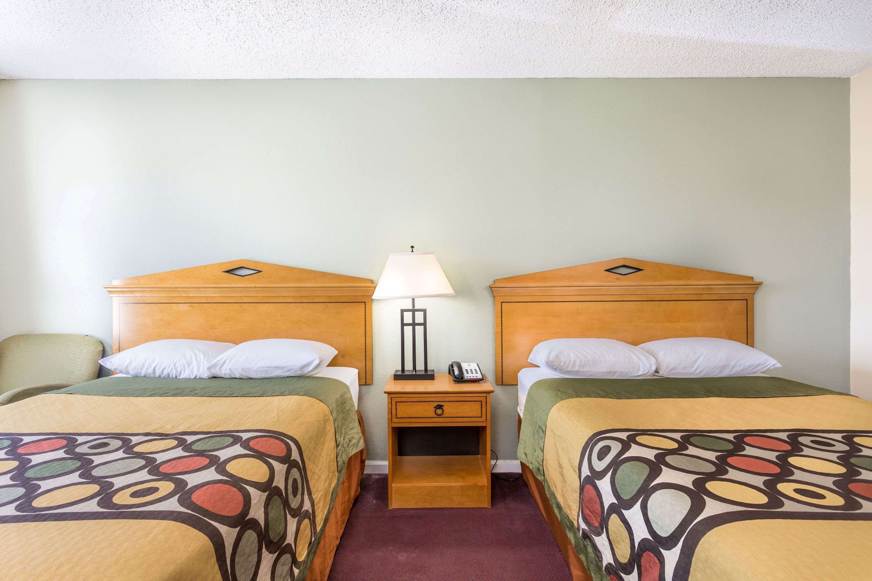 A hotel room with two beds, each with a wooden headboard, a nightstand with a lamp, and a telephone.