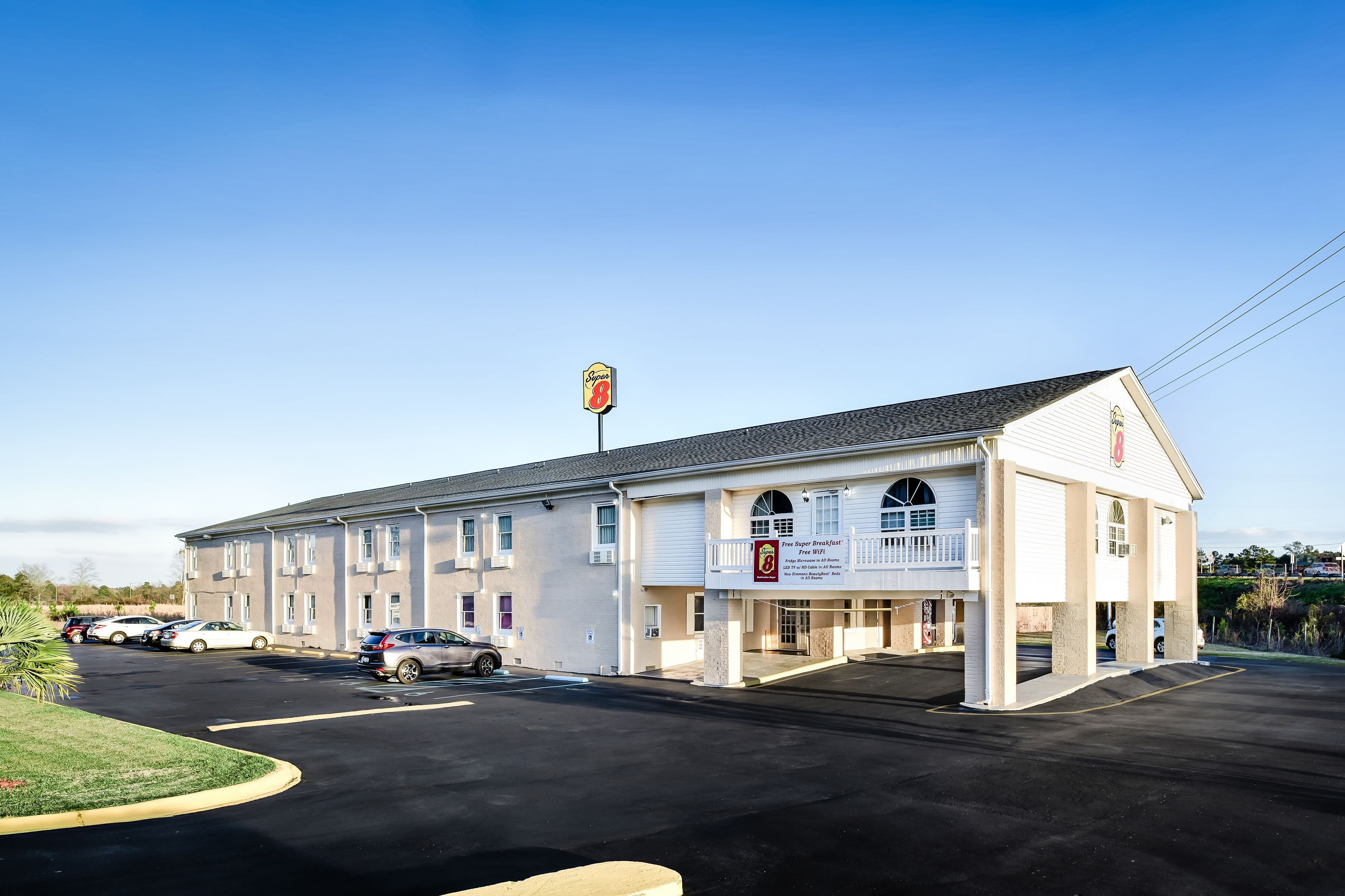 A motel with a large parking lot, a sign indicating it offers free parking, and a small outdoor area with a palm tree.