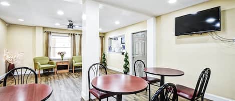 A dining area with round tables and chairs, a flat-screen TV mounted on the wall, and a ceiling fan.